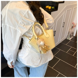 Dettaglio della mini borsa tote intrecciata con ciondolo a orsetto e tracolla sottile