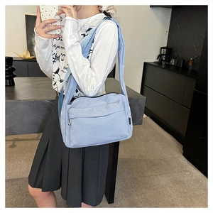 Detail of light blue nylon crossbody bag with silver zipper and wide shoulder strap