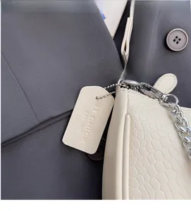 Close-up of cream crocodile pattern texture and silver chain strap on baguette bag