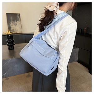 Detail of light blue nylon crossbody bag with zipper pockets worn by a model