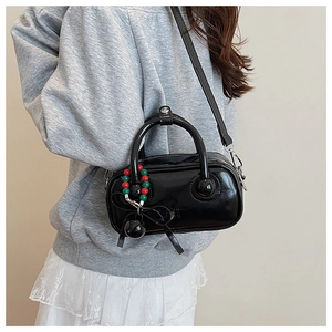 Detail of glossy black handbag with decorative red and green bead charm on a model