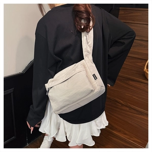 Detail of off-white nylon crossbody bag featuring a wide shoulder strap and front zip pocket