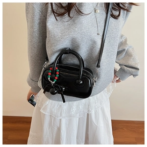 Detail of black patent leather mini boston bag with colorful beads and bow charm