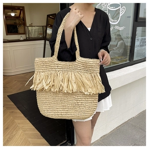Close-up of natural woven straw tote bag featuring layered tassel fringe and long straps