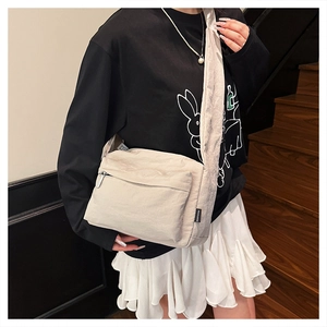 Detail of light beige nylon crossbody bag featuring textured fabric and front zip pocket