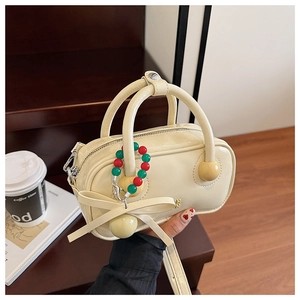 Detail of cream yellow PU Boston bag with beaded charms and bow accessory held by model