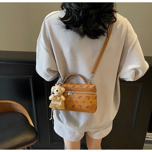 Detail view of brown crossbody bag with bear print and cute plush charm on a model