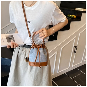 Détail du sac seau en denim et cuir marron porté par un mannequin avec fermeture à cordon