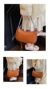 Detail of a brown crocodile pattern baguette bag with silver chain strap worn by a model