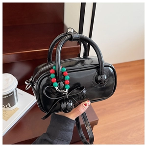 Detail of black patent leather mini boston bag with colorful beaded charm and bow