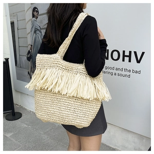 Close-up of beige woven straw tote bag with long tassel details in a street style view