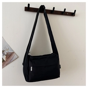 Detail of black nylon crossbody bag with dual zippers and silver metal hardware accents