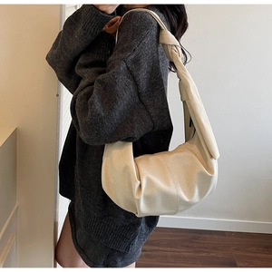 Close-up of cream-white crescent shoulder bag with knotted strap on casual outfit