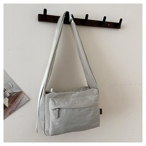 Vertical view of a light gray waterproof nylon messenger bag hanging on a wooden wall hook