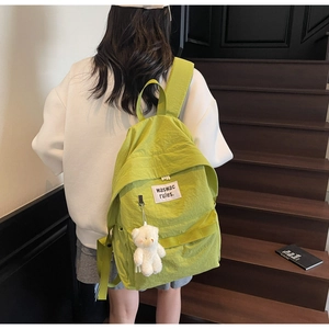 Detail of lime green nylon backpack with plush bear charm and white square label