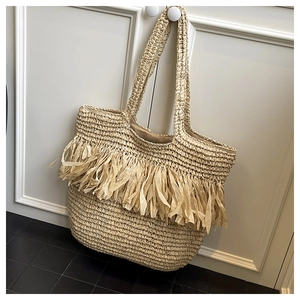 Detail of beige straw tote bag with woven fringe tassels hanging on a door handle