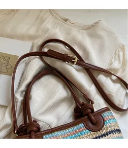 Detail of multi-color woven straw bag featuring brown leather trim and metal buckle strap