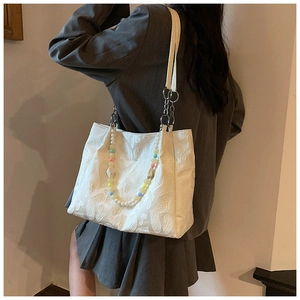Detail of white heart-embossed tote bag with colorful beaded charm and chain strap