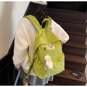 Detail of green backpack featuring a plush bear charm and white woven brand label
