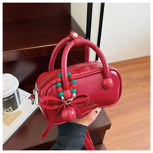 Detail of red glossy mini Boston bag with bow charm and brand embossing in a lifestyle setting