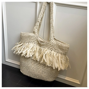 Detail of beige handwoven straw tote bag with long raffia tassels and dual shoulder straps