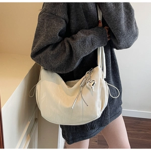 Detail of cream hobo bag featuring wide strap and stylish silver heart pendant detail