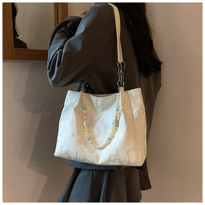 Detail view of white heart embossed tote bag with colorful macaron beaded charm on model