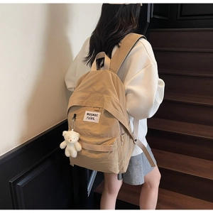 Detail of khaki nylon backpack with white plush bear pendant on wooden stairs