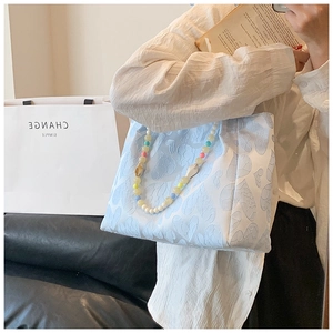 Detail of light blue heart pattern jacquard tote bag with colorful beaded handle straps