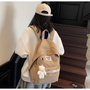 Detail of khaki nylon backpack with teddy bear charm on wooden stairs background