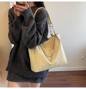 Detail of a cream pleated tote bag with pearl chain straps on a model in a mirror