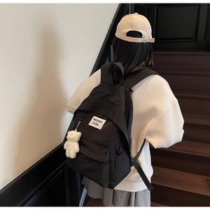 Close-up of black nylon backpack featuring white logo patch and cute plush bear charm