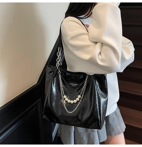 Detail of glossy black tote bag featuring chunky silver chains and pearl embellishments