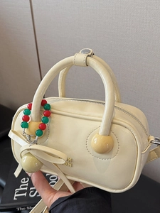 Chic cream leather boston bag with a matching bow and colorful beaded charm handle