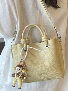 Chic yellow lychee leather bucket bag with twist handles and a cute cartoon charm
