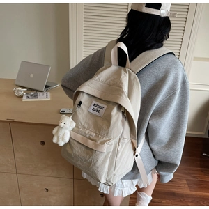 Detail of a beige nylon minimalist backpack featuring a cute white plush bear pendant