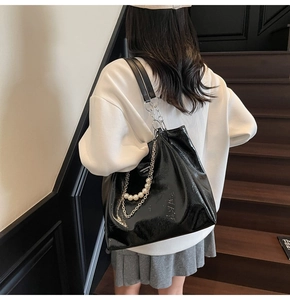 Detail of glossy black patent leather tote bag featuring pearl and silver chain charms