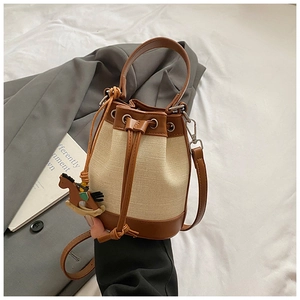 Gros plan du sac seau en toile avec finitions en cuir et breloque cheval sur costume