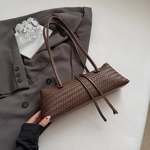 Macro detail of the woven dark coffee leather texture and shoulder strap on baguette bag