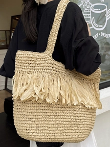 Large beige straw tote bag with fringe tassels for beach vacation shown on a female model