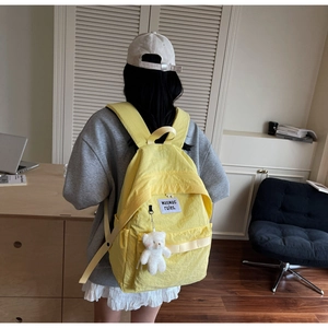 Detail view of a bright lemon yellow nylon backpack featuring a white plush bear charm