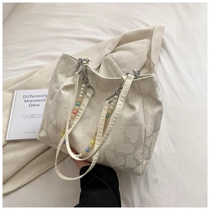 Detail of cream tote bag featuring embossed heart patterns and colorful beaded handle