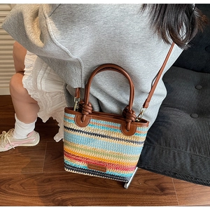 Close-up of a colorful striped woven bucket bag featuring brown leather shoulder straps