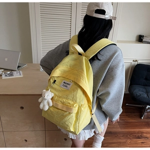 Detail of bright yellow nylon school backpack with a cute white plush bear keychain