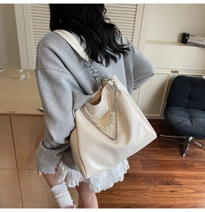 Close-up of ivory tote bag featuring glossy wrinkled texture, metal chains, and pearl accents