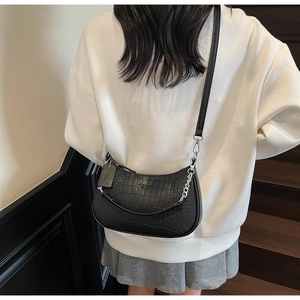 Close-up of a black croc-effect baguette bag with silver chain worn by a model