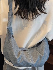 Minimalist light blue denim croissant bag with knotted strap shown on model shoulder