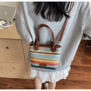 Detail of colorful woven straw bucket bag featuring a brown leather logo and strap