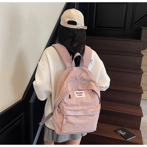 Detail of dusty rose nylon backpack with crinkled texture and white woven label
