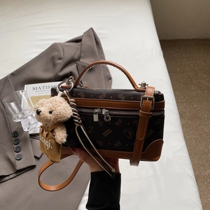 Close-up of brown box handbag with bear pattern, leather trim and plush bear charm